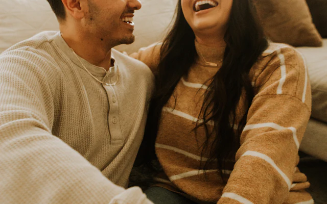 formato encontro para casais Casal sorrindo junto no sofá, à vontade para conversar sobre intimidade